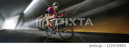 Banner. Cyclist wearing professional racing gear pedaling aggressively through tunnel, gripping handlebars tightly win aerodynamic pose. Banner. Cyclist wearing professional racing gear pedaling aggressively through tunnel, gripping handlebars tightly win aerodynamic pose. 122419483