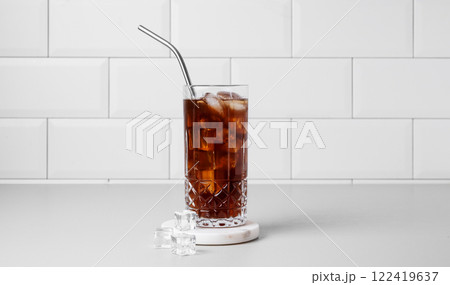 Cold brew coffee in a glass with ice and straw on a light table against a white brick background. Cold brew coffee in a glass with ice and straw on a light table against a white brick background. 122419637