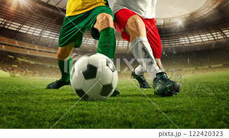 Soccer players uniforms competing for control of soccer ball on lush grass in stadium, spikes dig into turf as intensity increases. 122420323