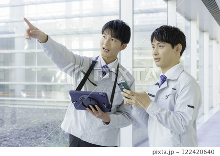作業着を着て通路で会話する若い男性2人 122420640
