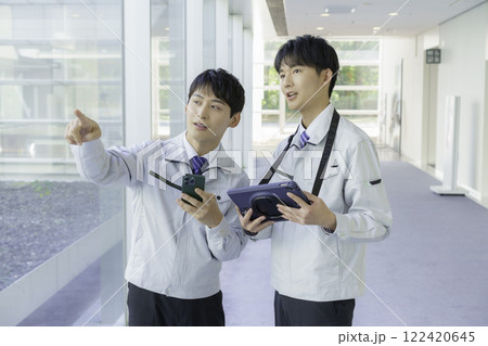 作業着を着て通路で会話する若い男性2人 作業着を着て通路で会話する若い男性2人 122420645