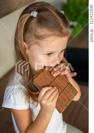 Little girl eating Dubai chocolate with pistachio paste and kataifi dough. Confectionery handmade sweets at home in the kitchen.  122421046