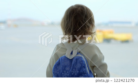 Preschooler girl waves hands looking at large airfield through window 122421270