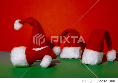 Santa hats on isometric green red background. Copy space for your text. Mock up for advertisement. Holiday Christmas composition. Minimalistic greeting card Santa hats on isometric green red background. Copy space for your text. Mock up for advertisement. Holiday Christmas composition. Minimalistic greeting card 122421466