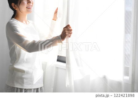 カーテンを開け日光を浴びるアジア人女性 122421898