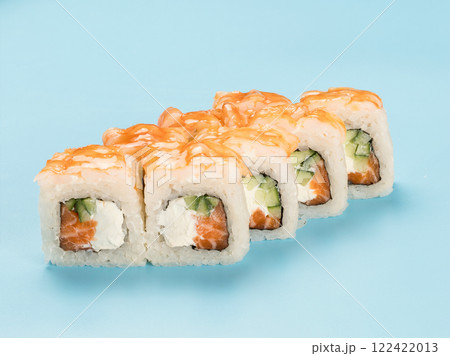Studio photography of Philadelphia Roll of velvety cream cheese, cucumber and salmon, wrapped in perfect seasoned sushi rice and fresh shrimp. Isolated on solid light blue background 122422013
