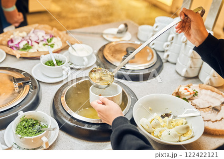Hands put a ladle of liquid soup. A delicious hot dish in cups with a variety of fresh vegetables and tender meat, simmered in a spicy broth. High quality photo 122422121