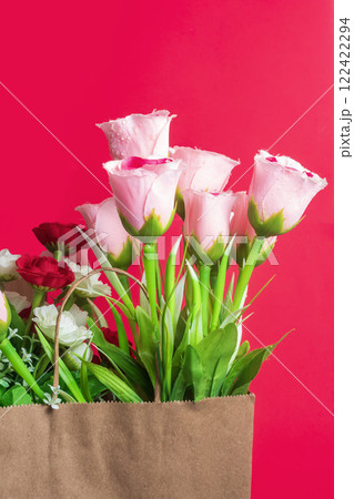 Beautiful bouquet of artificial flowers in a brown paper bag on a red background 122422294