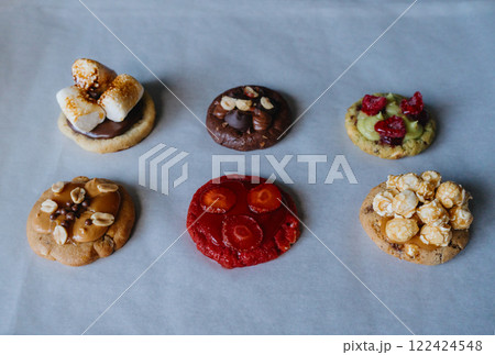 Homemade round cookies on baking paper with different toppings - raspberry, strawberry, pistachio, caramel, chocolate, peanuts, marshmallow, popcorn.  122424548