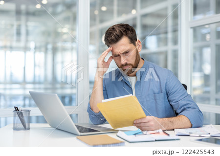 Bad news mail message about bankruptcy. Man upset inside office disappointed reading notification, holding envelope with letter. Dissatisfied worker inside office at workplace. 122425543