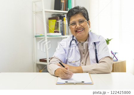 Asian doctor woman using a laptop computer and writing something on clipboard at hospital desk office, Healthcare medical concept. 122425800