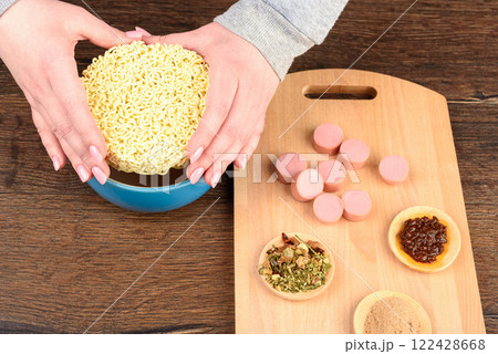 Female hands lowering dry instant noodles into a bowl for cooking. 122428668