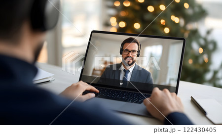 A person in a well-lit home office attending an online meeting on a laptop, wearing headphones and taking notes 122430405