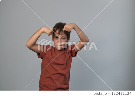 A young boy playfully flexes his arms, showing a determined expression as if demonstrating strength. This pose embodies confidence and the playful spirit of childhood exploration of identity. 122431124