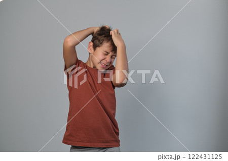 Frustrated boy clutches his head, a grimace of defeat on his face. Evokes the challenges and emotional growth experienced in childhood 122431125