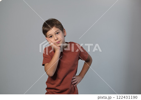 Thoughtful boy rests cheek in hand, looking pensive. Captures the essence of childhood contemplation and the purity of a young mind at rest. 122431190