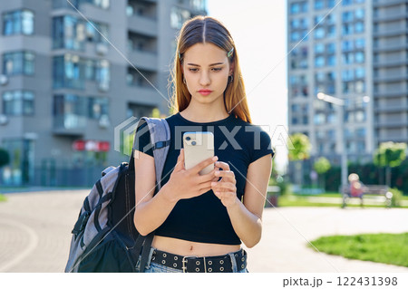 Young serious teenage female using smartphone, modern city background Young serious teenage female using smartphone, modern city background 122431398