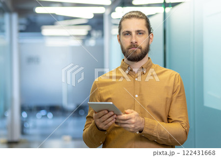 A confident young man in a professional office setting holding a tablet in hand. Ideal image for portraying technology, corporate environments, or modern workplace scenarios A confident young man in a professional office setting holding a tablet in hand. Ideal image for portraying technology, corporate environments, or modern workplace scenarios 122431668