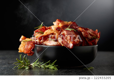 Fried bacon in a black dish with rosemary on a black background. Fried bacon in a black dish with rosemary on a black background. 122433205