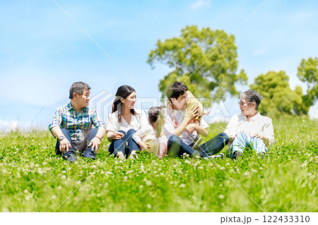青空の草原に座る三世代家族 122433310
