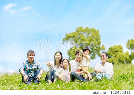 青空の草原に座る三世代家族 122433311