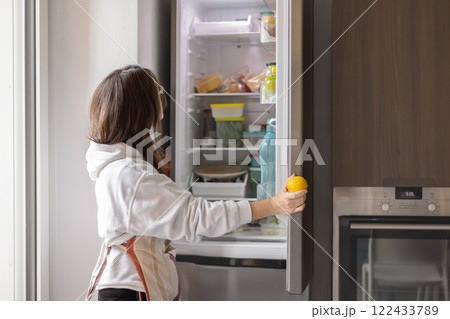 Young woman opening refrigerator in modern kitchen holding lemon, healthy food concept Young woman opening refrigerator in modern kitchen holding lemon, healthy food concept 122433789