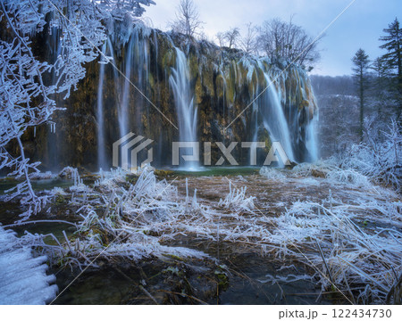 Winter waterfall, lake, frozen trees with icicles in cold evening 122434730