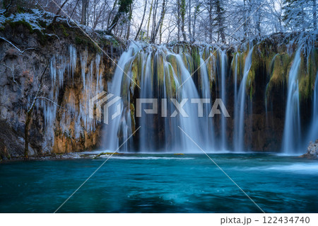 Winter waterfall, lake, frozen trees with icicles in cold evening 122434740