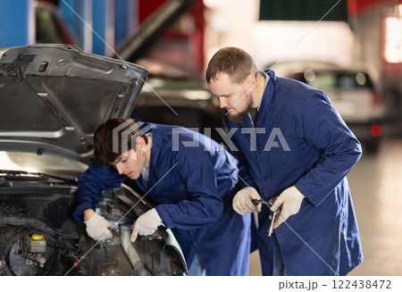 Two auto mechanics work together to diagnose an engine under the hood of a car in repair shop Two auto mechanics work together to diagnose an engine under the hood of a car in repair shop 122438472