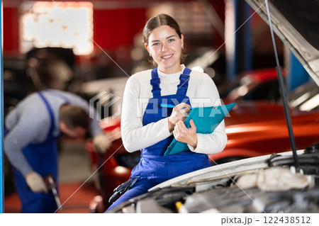 Female car service worker keeps records of work performed by auto mechanics in car service station - makes notes on paper Female car service worker keeps records of work performed by auto mechanics in car service station - makes notes on paper 122438512