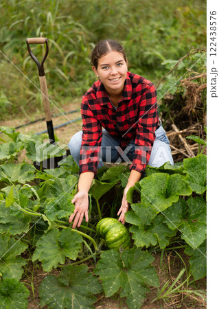 During gardening, girl in plaid shirt found large ripe pumpkin among leaves. During gardening, girl in plaid shirt found large ripe pumpkin among leaves. 122438576