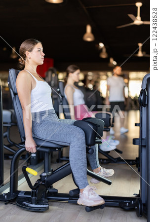 Slender athletic girl work out muscles of legs and thighs on simulator in fitness club Slender athletic girl work out muscles of legs and thighs on simulator in fitness club 122438628