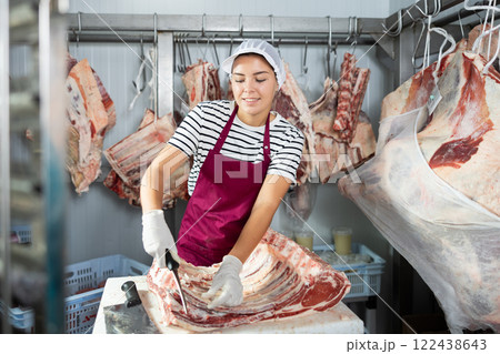Female employee of local butcher shop divides large huge piece of meat with knife 122438643