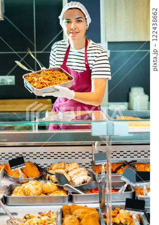 Salesgirl offering ready-to-eat meat stew in deli section of supermarket 122438662