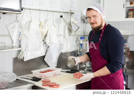 Male food company employee prepares raw meat cutlets using special equipment Male food company employee prepares raw meat cutlets using special equipment 122438818