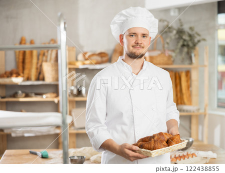 Baker in white uniform stands behind counter in small private bakery offering hot croissants 122438855