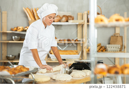Young female baker shaping dough into baguette in bakery 122438871