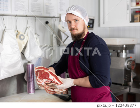 Butcher holding slab of beef rib steaks in shop processing room Butcher holding slab of beef rib steaks in shop processing room 122438877