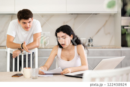 Sad girl works with laptop and paper documents and listens to reproaches of young guy Sad girl works with laptop and paper documents and listens to reproaches of young guy 122438924