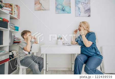 young female speech therapist in medical scrubs engaging in articulation exercises with boy in bright therapy room, concept of speech development, child psychology 122439559
