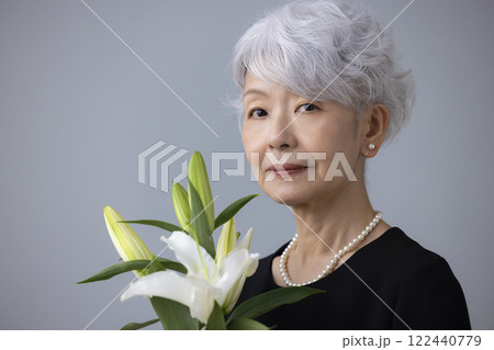 喪服を着て百合の花を持っているシニア女性 122440779