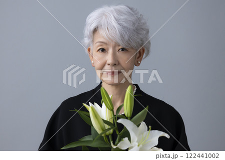 喪服を着て百合の花を持っているシニア女性 122441002