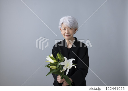 喪服を着て百合の花を持っているシニア女性 122441023