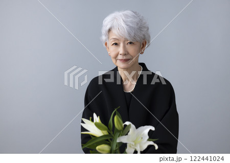 喪服を着て百合の花を持っているシニア女性 122441024