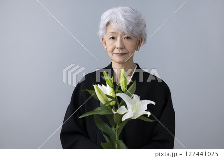 喪服を着て百合の花を持っているシニア女性 122441025