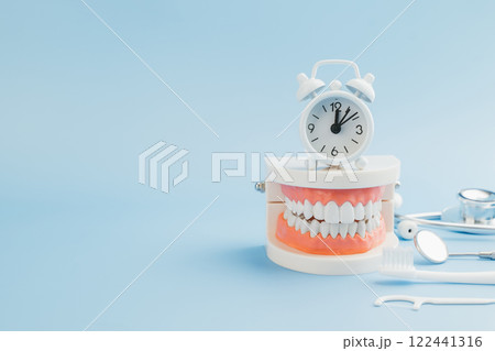 A Dentist presents a teeth model with a white alarm clock, emphasizing oral care, dentistry tools A Dentist presents a teeth model with a white alarm clock, emphasizing oral care, dentistry tools 122441316