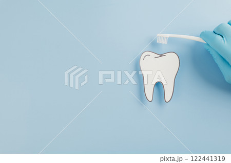 A gloved doctor holds a toothbrush with a paper tooth for Dentist Day A gloved doctor holds a toothbrush with a paper tooth for Dentist Day 122441319