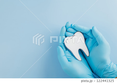 A dentist gloved hands hold a tooth paper cutout on blue for Dentist Day A dentist gloved hands hold a tooth paper cutout on blue for Dentist Day 122441325