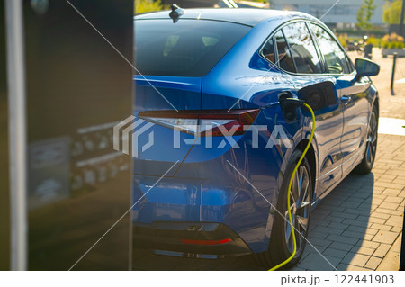 Electric vehicle connects to a charging station in an urban environment on a sunny day Electric vehicle connects to a charging station in an urban environment on a sunny day 122441903
