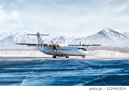 White passenger turboprop airliner on the winter airport apron on the background of high picturesque mountains 122442824